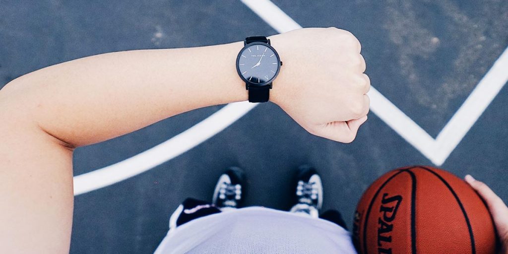A person holding a basket ball and checking their watch