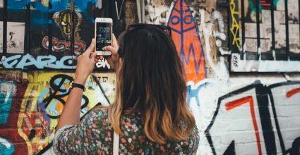 A person taking photos on a phone of graffiti on a wall